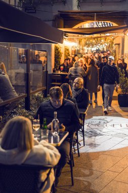 Perpignan, Fransa 'da aydınlık bir şehir caddesinde dar ve açık bir bar terasında oturan insanların resimlerini çeken bir yazı. Sahne, şehir gece hayatını, kışın sosyalleşmeyi ve sicim ışıkları altındaki şenlikli atmosferi ön plana çıkarıyor..