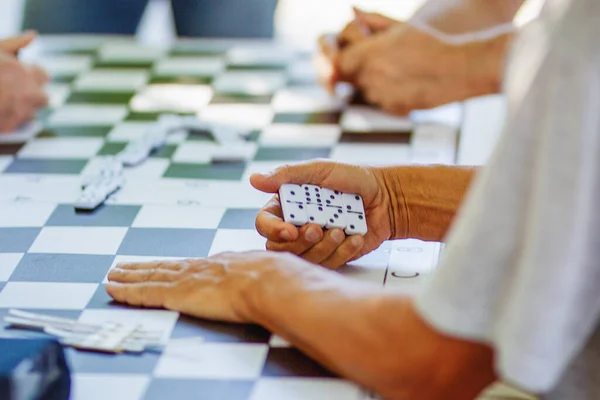 Elderly people playing domino. Image of dominos on a wooden table in the middle of a game with hand placing a tile