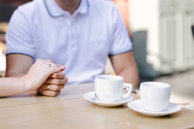 Bugün ve her gün evlen benimle. Birbirini tutan altın yüzüklü bir çiftin resmi, düğün fotoğrafı. Ahşap masada iki beyaz kahve fincanı var. Seçici Odaklanma