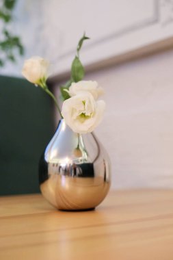 Tahta masadaki gümüş vazoda duran küçük, narin, beyaz çiçekler pembe taş duvarda duruyor. Boşluğu en düşük düzeyde kopyala. Kartpostal, metin, tasarım için şablon Kadın Günü, Anneler Günü.