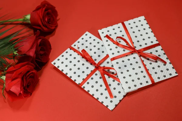 3 red roses with 2 gifts envelopes, red ribbons, certificates, invitation card inside. Craft concept. Red on the red background. Copyspace for text. Weddig, ceremony concept, holidays and surprises.