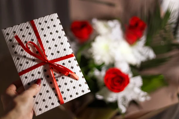 ホワイト ギフト 封筒に赤いリボンの証明書女性の手札に招待状 工芸の概念 ウェディグ式のコンセプト休日の驚き 咲く花々の背景 — ストック写真