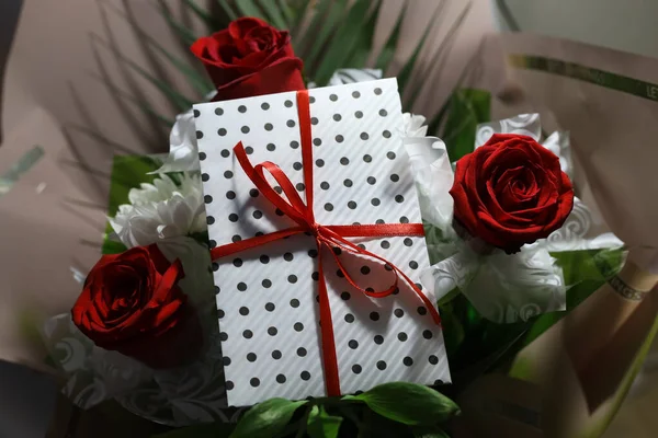 3 red roses  bouquet with gift envelope, red ribbons, white paper for certificates, invitation card inside. Craft concept. Red on the red background.   Weddig, ceremony concept, holidays, surprises.