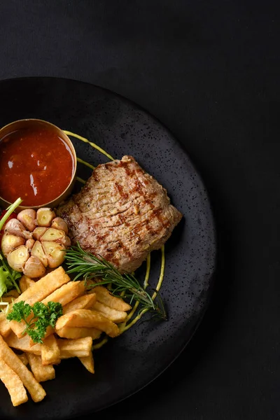 Patatesli ızgara biftek, sebze ve siyah arka planda salata.