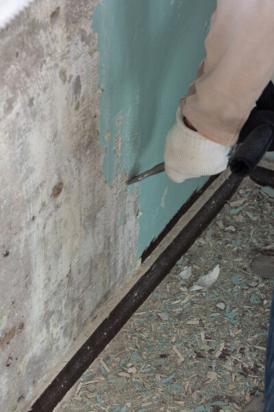 Рабочий убирает старую краску с бетонной стены
