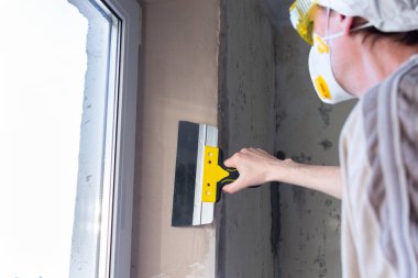 Apartman dairesinde tamirat, pencere aralıklarını güçlendirme, erkek müteahhit macunu macun bıçağıyla düzleştiriyor.