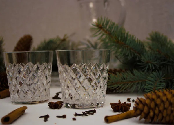 Utensilios de cristal sobre un fondo blanco junto a la mentira especias para el vino caliente y ramas de abeto en el fondo —  Fotos de Stock