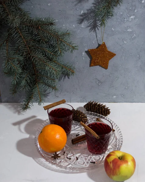 Glasses with mulled wine on a glass tray with apples, oranges, cinnamon, badyan, cloves on a white background. — Stock Photo, Image
