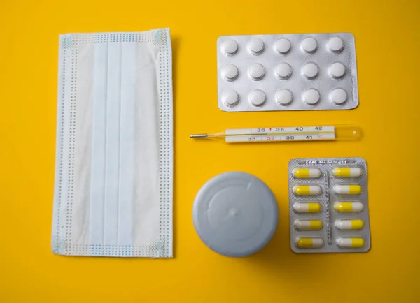 Skyddande medicinsk mask, tabletter, termometer på gul bakgrund — Stockfoto