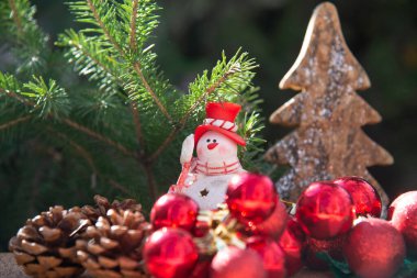 Noel kardan adamı, kırmızı Noel süslemeleri ve yeşil bir Noel ağacının arka planında koniler. Noel arkaplanı