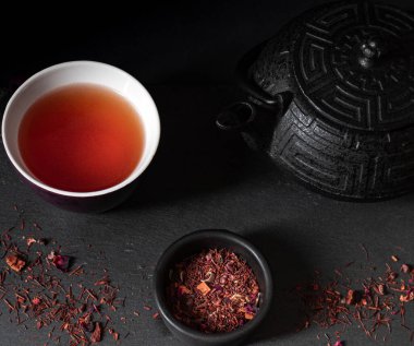 Siyah arka planda kırmızı çay fincanı çaydanlığı ve kuru çayıyla.