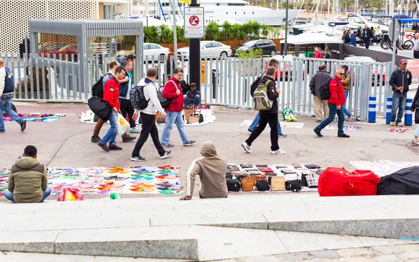 BARCELONA, İspanya - 30 Nisan 2016: Göçmenler mallarını Port de Barcelona yakınlarındaki bir sokakta, arka plan ticaretini yasaklayan bir tabela önünde battaniyelerden satıyorlar