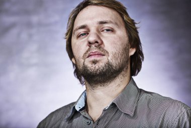 Eflatun bir arka planda çizgili gömlekli kibirli orta yaşlı bir adamın stüdyo portresi.