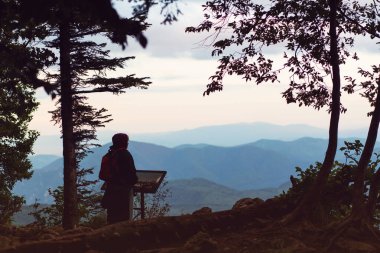 Kırmızı sırt çantalı bir turist kız vadiye bakan bir dağın tepesindeki izleme platformunda duruyor. Plato Lago-Naki, Adygea, Rusya