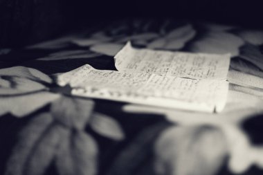 Rusça yazılmış iki sayfa mektup yatağın üzerinde yatıyor. Siyah beyaz fotoğraf, tonlu..