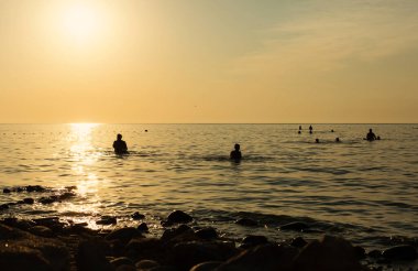Gün batımında denizde yüzen insanların siluetleri. Rusya, Azov Denizi, Krasnodar Bölgesi, Yeysk.
