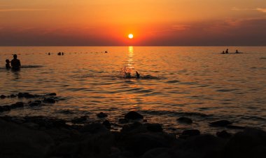 Gün batımında denizde yüzen insanların siluetleri. Rusya, Azov Denizi, Krasnodar Bölgesi, Yeysk.