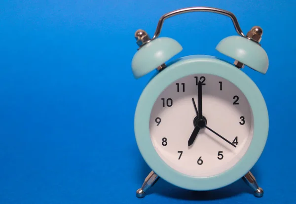 Un pequeño reloj despertador azul sobre un fondo azul, en el dial de los cuales 07: 00. Salida de la mañana al trabajo. Fotos De Stock Sin Royalties Gratis