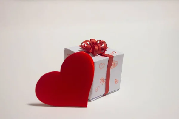 Corazón rojo y una caja con un regalo y una cinta roja sobre un fondo blanco. —  Fotos de Stock
