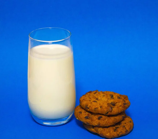 Mavi arka planda bir bardak süt ve üç yulaflı bisküvi — Stok fotoğraf