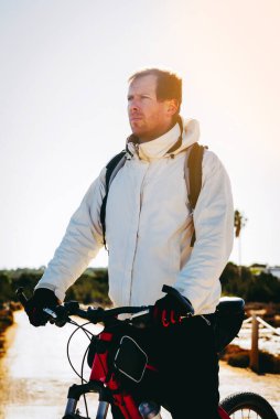 Kırmızı bisiklete binen genç adam, kırsalda güneşin doğuşunu izliyor.