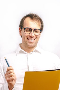 Gözlüklü genç adam elinde mavi kalemle sarı bir klasörde rapor okuyor. Beyaz arkaplan.