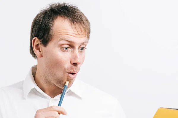 Sarı klasörü okuyan ve elinde kalem tutan genç adam şaşırdı. Beyaz arka plan..