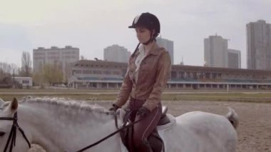 Genç bayan binici, açık havada kumlu parkta at biniciliği alanında yürüyor. Açık havada at eğitmek, binicilik sporu.. 