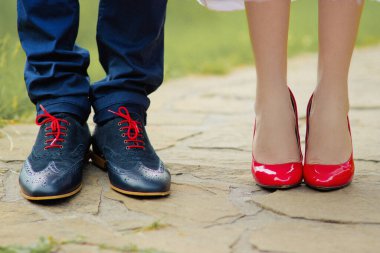 Gelin ve damat güzel ayakkabılarla parkta kaldırımda duruyorlar.
