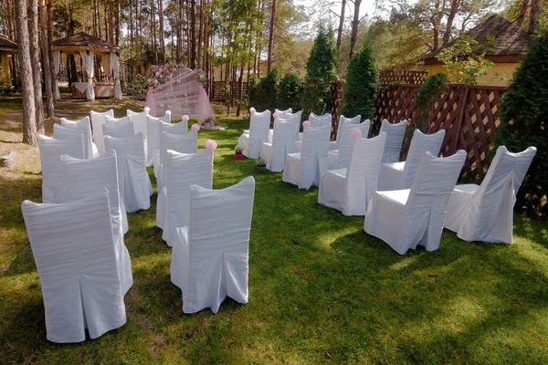 Outdoor wedding ceremony, chairs decorated with flowers and ribbons stand in rows on the grass — Stock Photo, Image