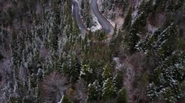 Dağlardaki virajlı bir yolun hava manzarası. Arabalar yavaş ilerliyor, karlı bir hava. Kuşların gözü dağlardaki kıvrımlı yolda.