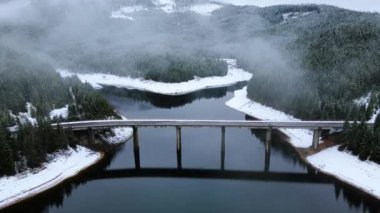 Kışın dağ gölü üzerindeki bir köprünün havadan görünüşü. Kamera köprüyü çerçevede tutmak için aşağı doğru eğiliyor. Köprünün insansız hava aracı görüntüleri