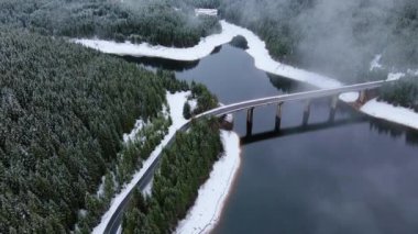 Kışın yol ve köprüyle bir dağ gölü manzarası.
