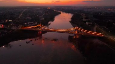 Gün batımında nehri geçen parlak bir köprünün insansız hava aracı görüntüleri. Geri geri uçan ve irtifa toplayan İHA köprüyü odakta tutuyor. Gün batımında aydınlatılmış köprü İHA 'dan çekiliyor..
