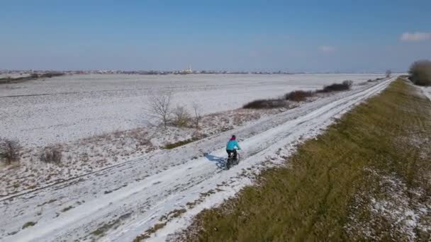 雪に覆われた牧草地でマウンテンバイクのトレーニングのドローン映像 後方右側からのライダーに続くドローンは ビューに彼を維持します 冬のバイカー訓練の空中ビデオ — ストック動画