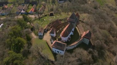 Romanya 'nın Brasov kentindeki Viscri köyündeki ortaçağ güçlendirilmiş bir kilisenin hava görüntüleri. Kalenin etrafında saatçi karşıtı daireler çizerken daha yüksek bir açıdan insansız hava aracı atışı..