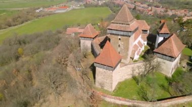 Romanya 'nın Brasov kentindeki Viscri köyündeki ortaçağ güçlendirilmiş bir kilisenin hava görüntüleri. Kalenin etrafında daireler çizerken daha yüksek bir açıdan insansız hava aracı atışı..