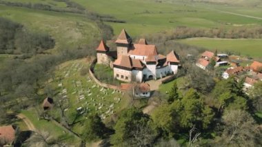 Romanya 'nın Brasov kentindeki Viscri köyündeki ortaçağ güçlendirilmiş bir kilisenin hava görüntüleri. Kalenin etrafında daireler çizerken daha yüksek bir açıdan insansız hava aracı atışı..