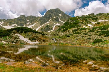 Yazın dağlardaki buzul gölü manzarası. Arka planda dağ zirveleri olan bir göl manzarası. Hava güneşli, hava bulutlu.. 