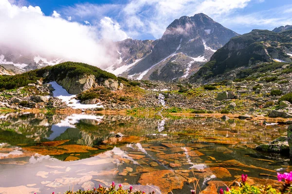 Yazın dağlardaki buzul gölü manzarası. Arka planda dağ zirveleri olan bir göl manzarası. Hava güneşli, hava bulutlu.. 