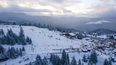 Aerial view of a small resort on top of the mountain in winter season at sunset. Photography was shot from a drone at a higher altitude. Aerial view of a resort in winter at sunset