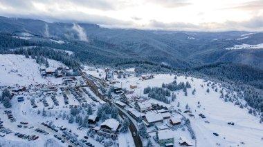 Aerial view of a small resort on top of the mountain in winter season at sunset. Photography was shot from a drone at a higher altitude. Aerial view of a resort in winter at sunset