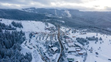 Aerial view of a small resort on top of the mountain in winter season at sunset. Photography was shot from a drone at a higher altitude. Aerial view of a resort in winter at sunset