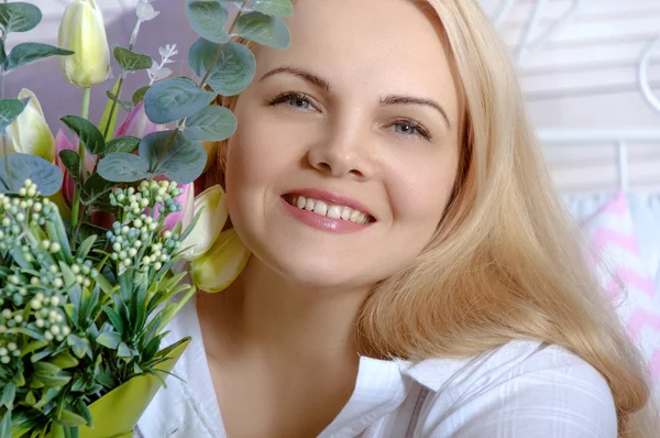 Flicka sitter i sängen med en bukett blommor. — Stockfoto