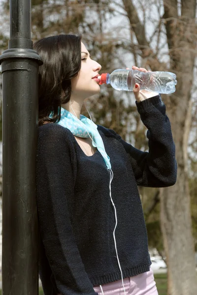 Dívka pití vody a poslechu na sluchátka — Stock fotografie