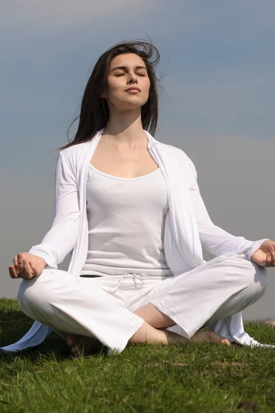 Menina realiza ioga na colina contra o céu azul . — Fotografia de Stock