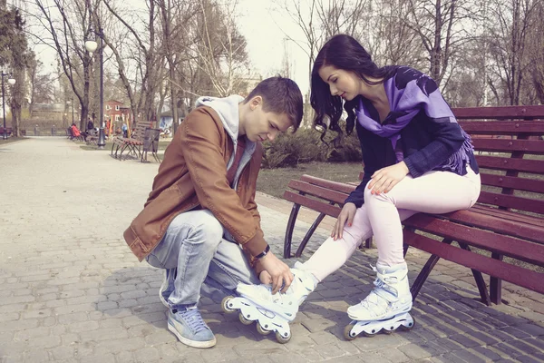 Garçon aide la fille à porter des patins à roulettes . — Photo