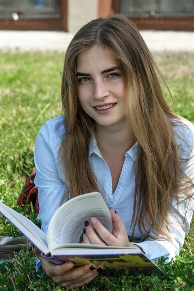 Menina lê um livro enquanto deitado na grama — Fotografia de Stock