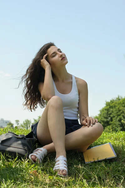 Девушка сидит на траве после школы — стоковое фото