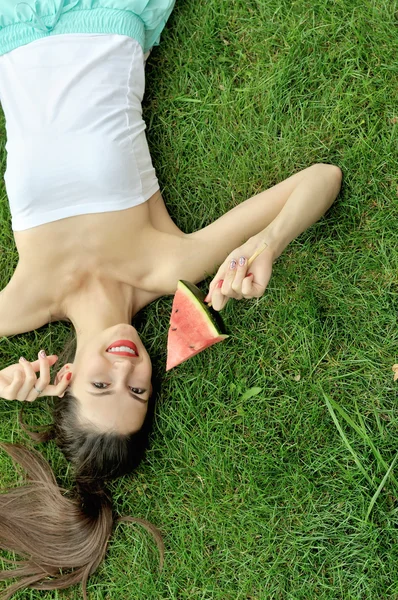 Menina deitada na grama com uma fatia de melancia — Fotografia de Stock